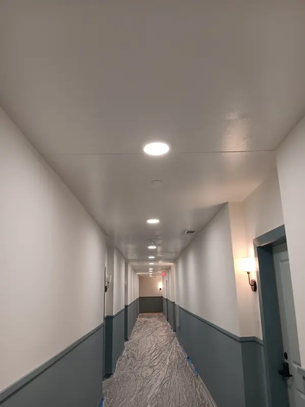 Long corridor painted white above a gray-blue lower wall, floor papered to protect it mid-job
