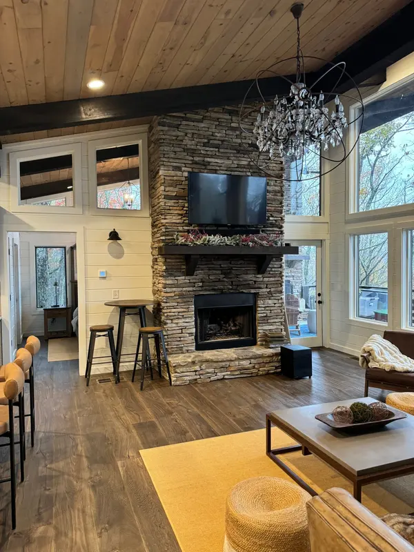 Living room with a stacked stone fireplace, plank ceiling and dark-painted beams