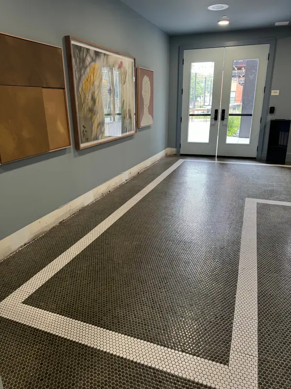 Commercial lobby with a dark tiled floor bordered in pale mosaic, gray walls and glass entry doors