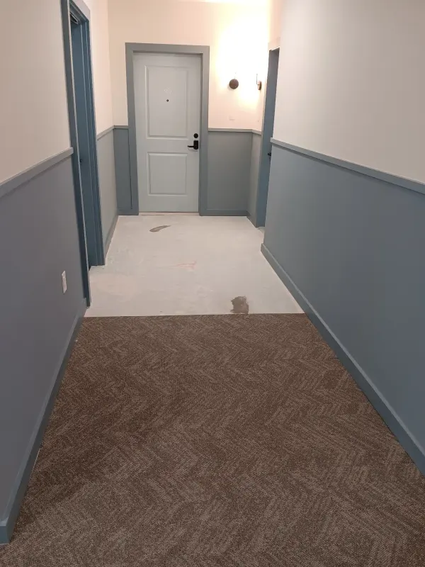 Corridor painted white above a blue-gray lower wall, patterned carpet part-laid