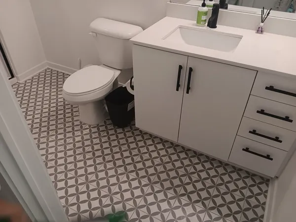 White vanity and toilet over a patterned gray geometric tile floor