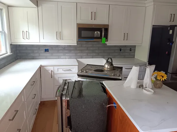 White shaker kitchen with gray subway tile, quartz tops and a cooktop set into the run