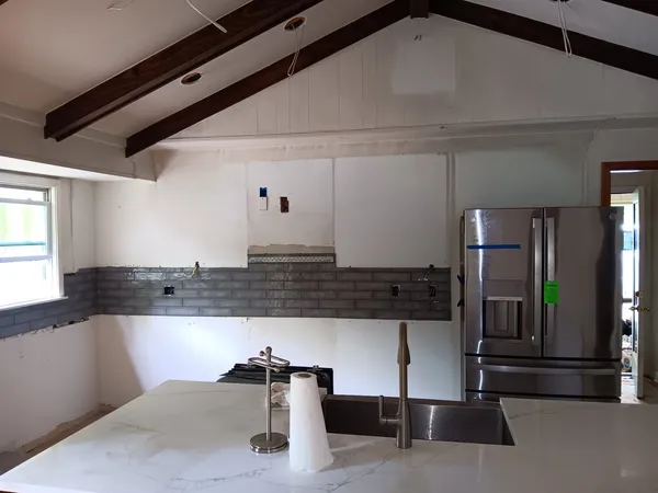 Vaulted room with exposed beams, a white island with a stainless sink and a slate backsplash