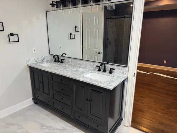 Dark double vanity with a marble top, twin basins and a framed mirror