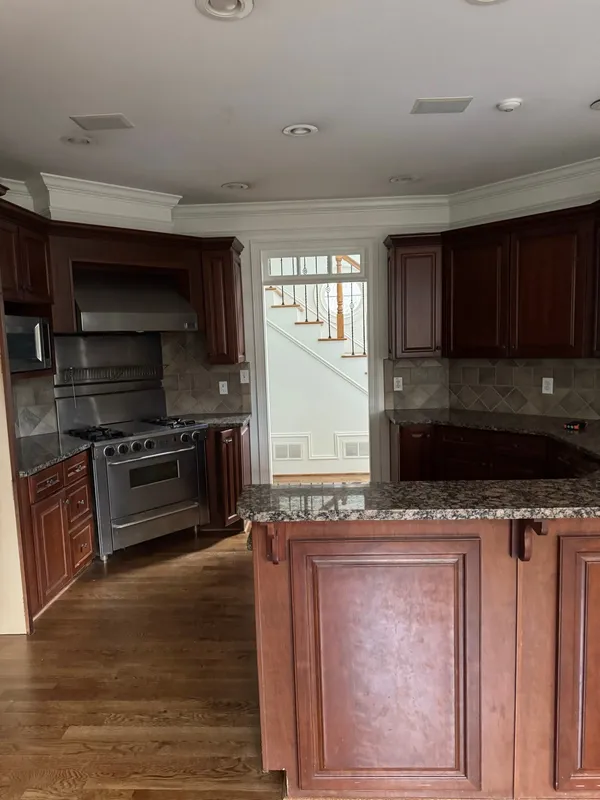 Dark cherry kitchen with a stainless range and hood, granite tops and a raised island