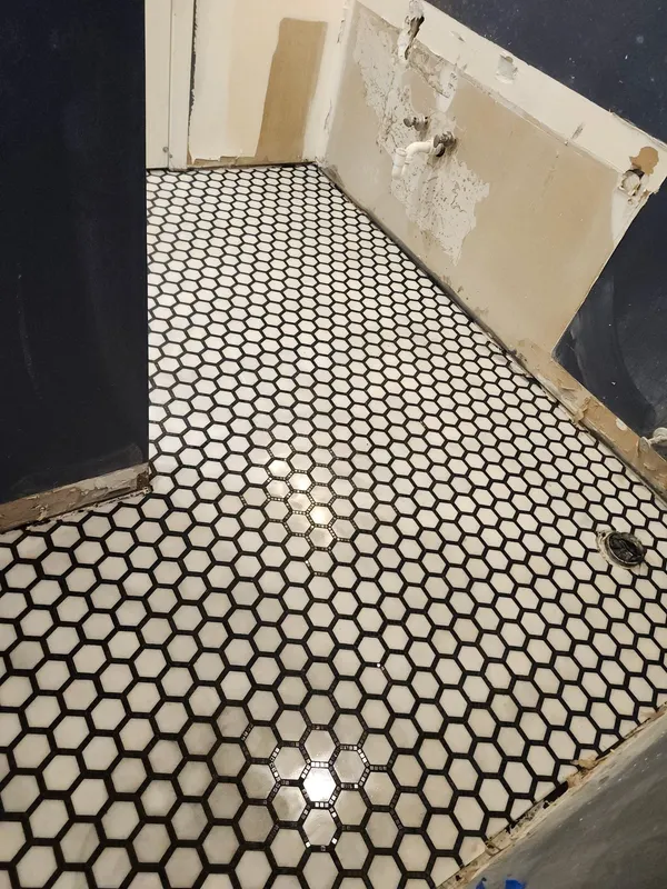 Black and white hexagonal mosaic floor newly laid, walls stripped back ready for finishing