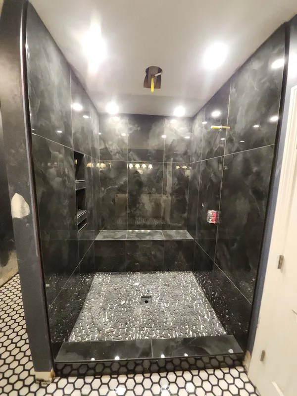 Walk-in shower lined in large dark marble-effect tile with a lit niche and pebble floor