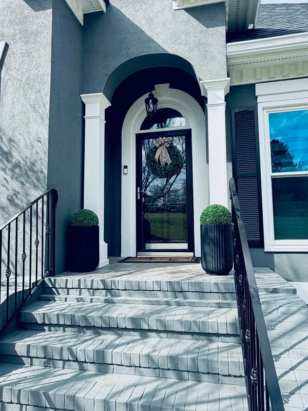 Navy-gray stucco entry with an arched head, white columns and a black door